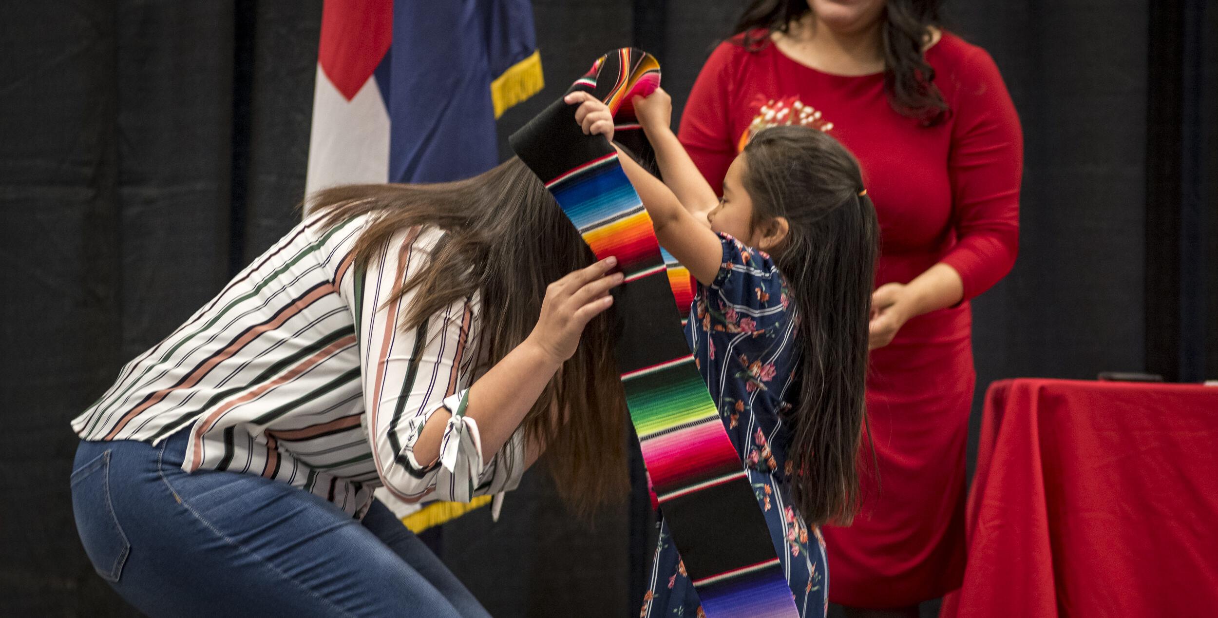 A little girl putting the latinx stole on her mom.