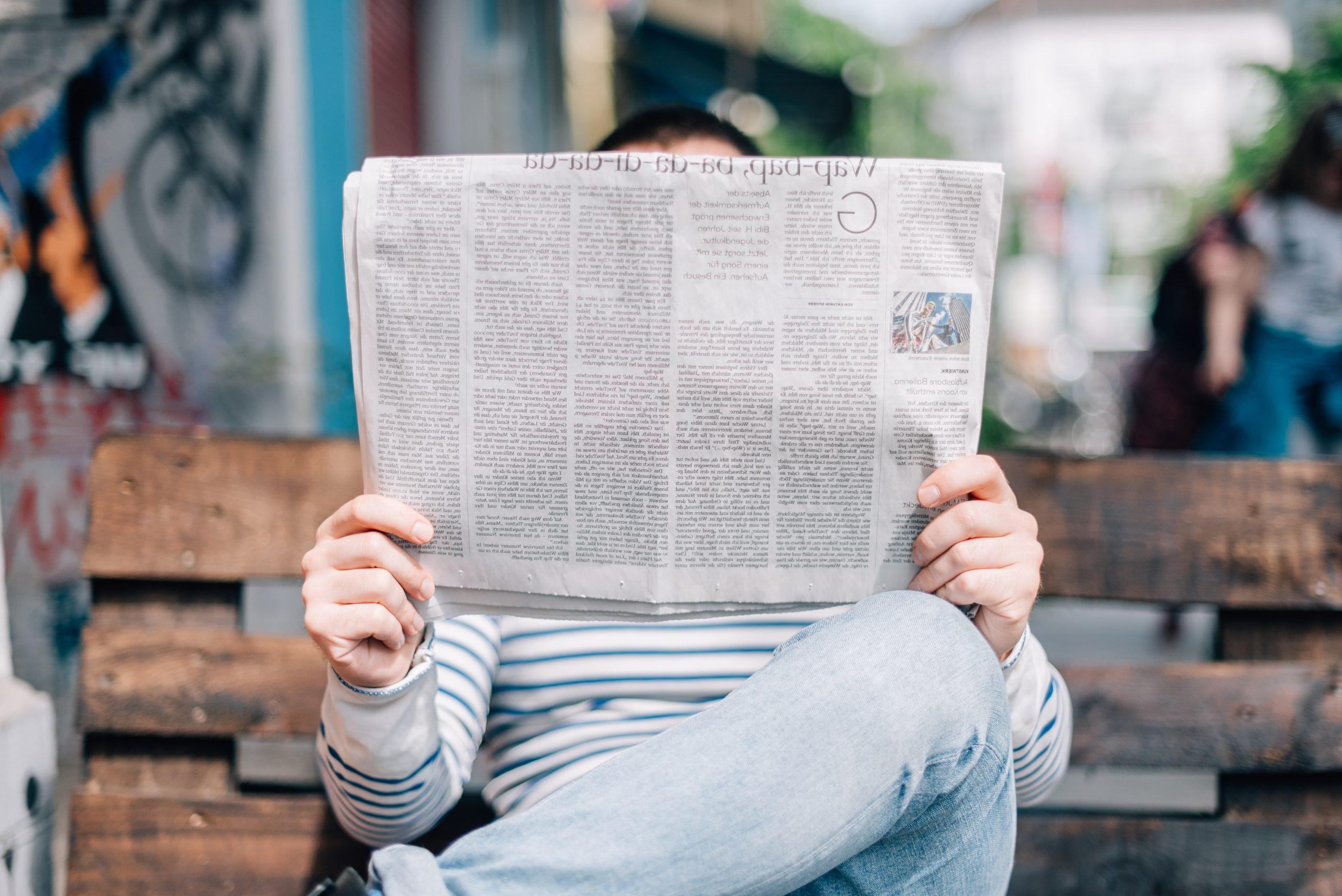 A Person sitting on bench reading a newspaper