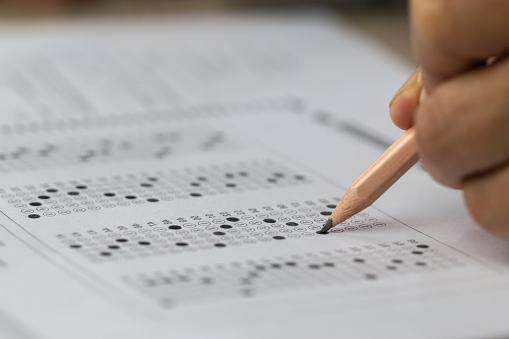 A hand holding a pencil filling in an exam bubble answer sheet