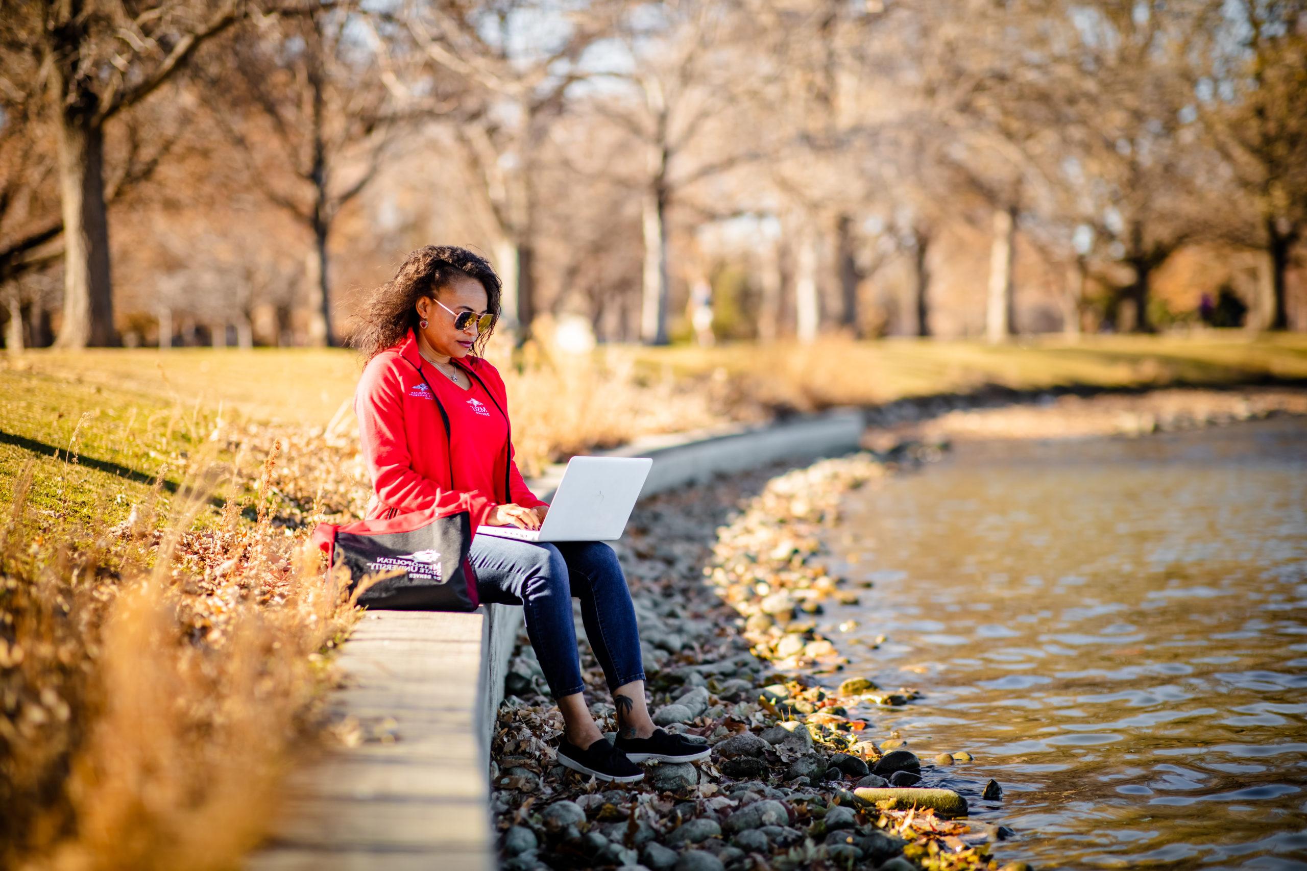 Karena Beckham in MSU Denver swag, working on a laptop in City Park.