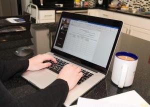 Close up of hands typing on a laptop computer in home kitchen.