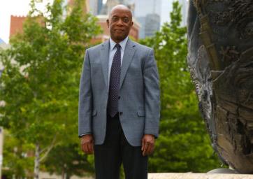 Russell Noles standing next to the statue in front of the Student Success Building with the Tivoli and trees in the background.