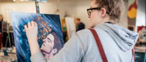 Looking over the shoulder of a student painting on an easel.