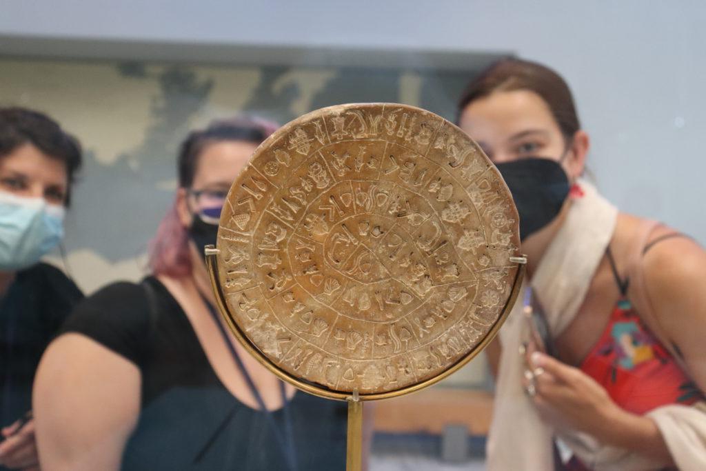 Students in the background regard a circular stone with ancient writing.