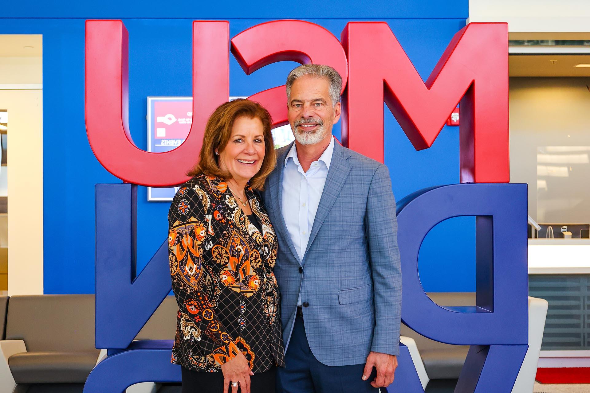 Ferd and Christy Belz standing in front of the red and blue MSU Denver sign