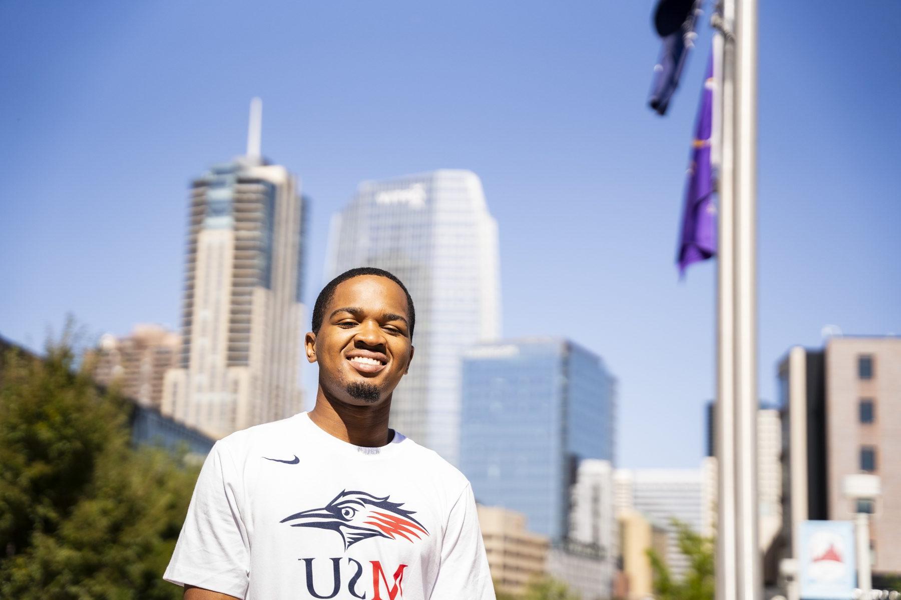 Photo of one of the MSU Denver MISTERs standing outside on Auraria Campus with downtown Denver in the background.