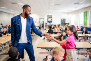 Dr. Rashad Anderson exchanging a handshake with a young female student in an elementary school cafeteria.