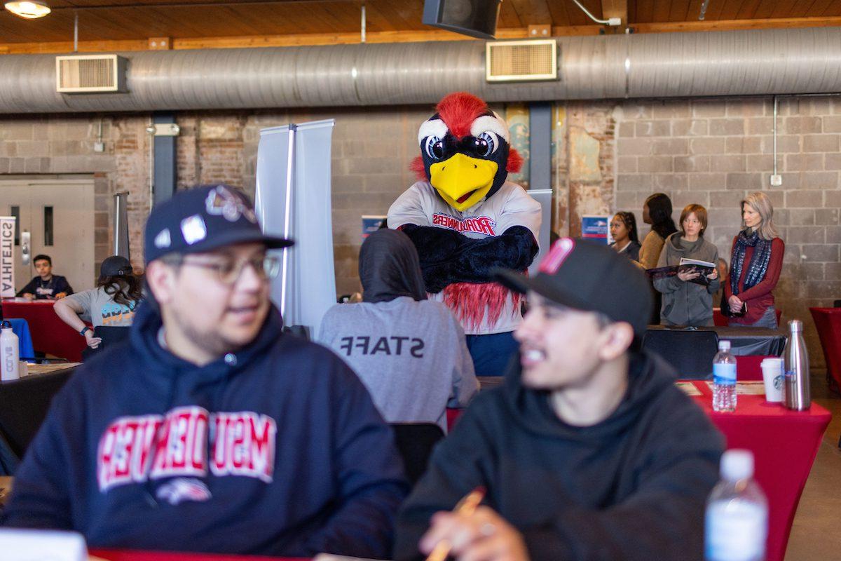 Two students in the foreground with Rowdy the Roadrunner posing in the background